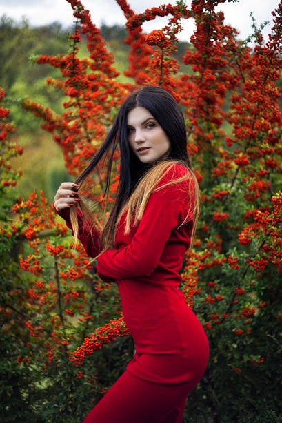 sexy red dressed girl posing in front of red berries tree playing with her black long hair