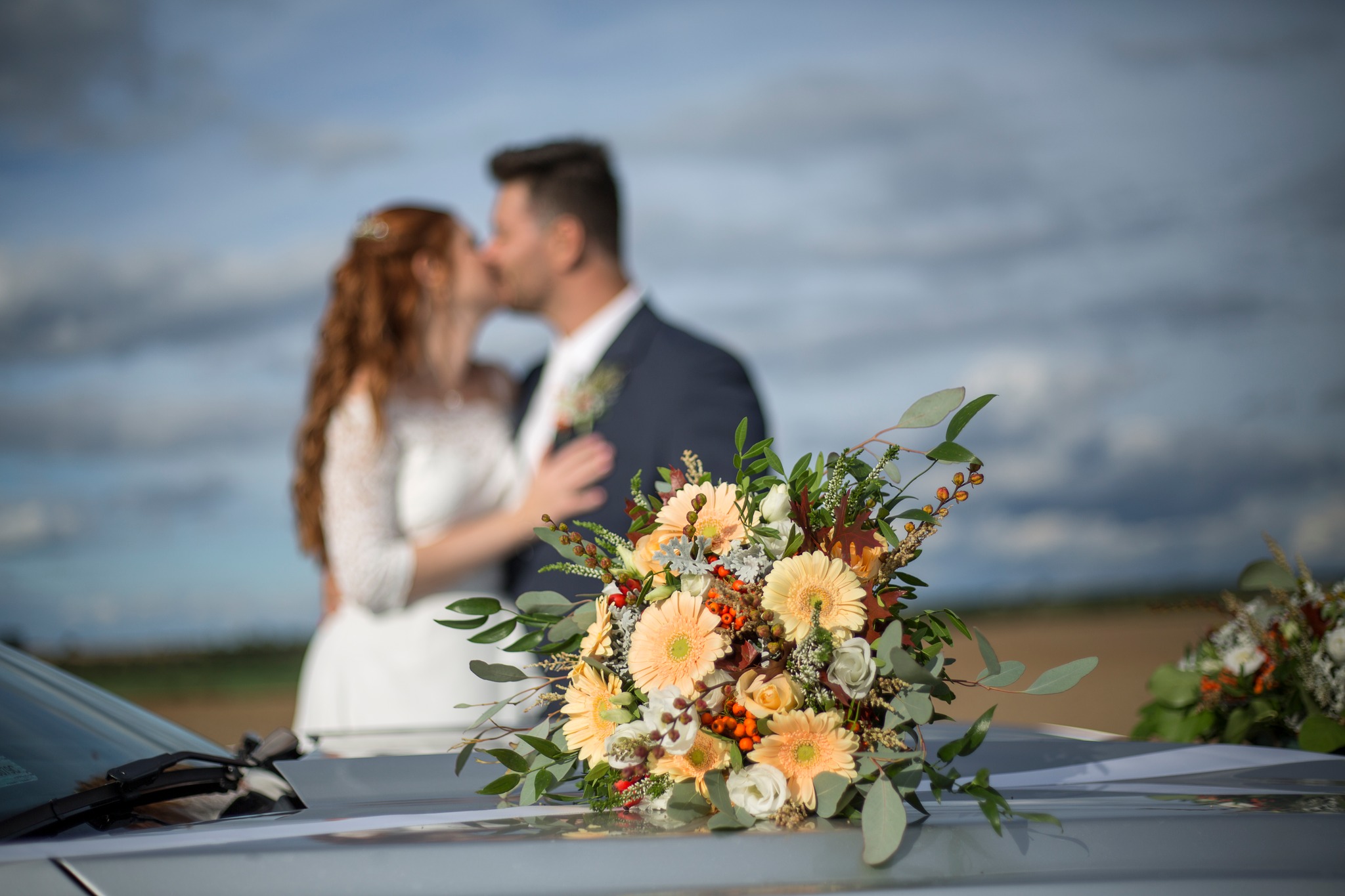 detail of wedding flowers and kissing bride and groom in background